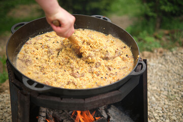 Cooking porridge with meat in a cauldron on an open fire, in nature