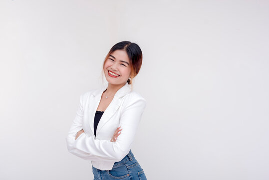 A happy and beaming young woman looking and smiling at the camera with arms crossed. Isolated on a white background.
