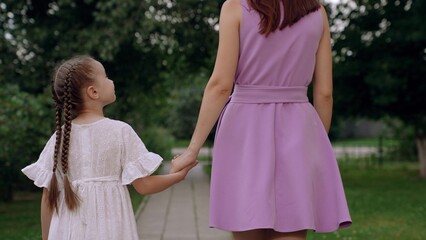 Fototapeta na wymiar Little daughter looks at mother joining hands walking across city park