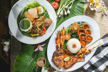 Balinese cuisine of seafood contains baked fish, clamp, and prawn served with another amin course of tempe and tahu with indonesian dressing vegetables on the table covered with banana leaf.
