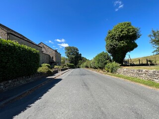 Fototapeta na wymiar Rural scene, with houses, stone walls, and old trees, set against a vivid blue sky near, Roundell Drive, West Marton, UK
