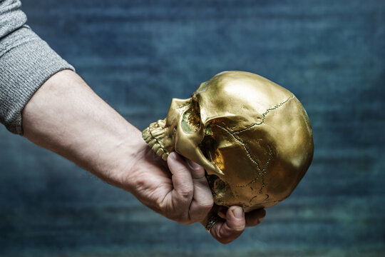 A male hand holding a gold painted skull