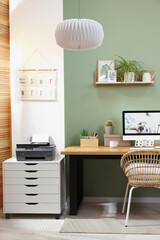 Stylish workplace with computer, printer and houseplant near olive wall at home