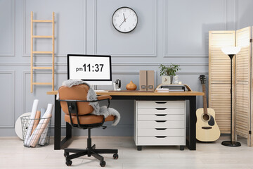 Stylish workplace with computer, houseplant and stationery on wooden desk near grey wall at home