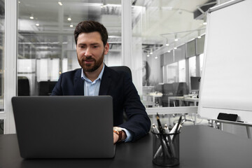 Man working on laptop at black desk in office. Space for text