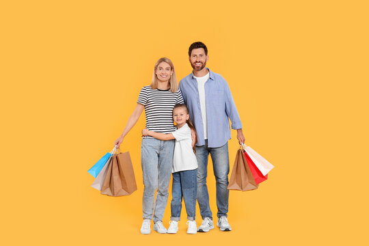 Family Shopping. Happy Parents And Daughter With Paper Bags On Orange Background