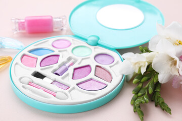 Obraz na płótnie Canvas Decorative cosmetics for kids. Eye shadow palette, accessories and flowers on pink background, closeup