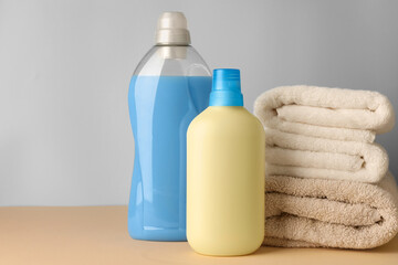 Bottles of fabric softener and stacked clean towels on pale yellow table against light grey background, space for text