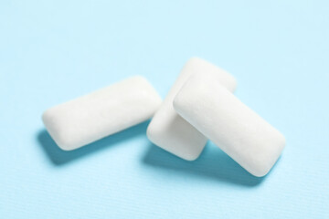 Tasty white chewing gums on light blue background, closeup