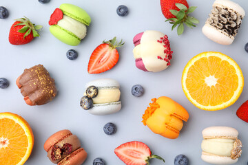 Delicious macarons, fruits and berries on light blue table, flat lay