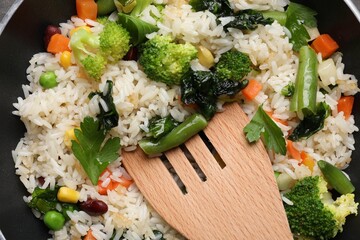 Tasty fried rice with vegetables and wooden spatula in frying pan, top view