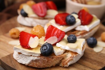 Tasty sandwiches with brie cheese, fresh berries and almond flakes on wooden board, closeup
