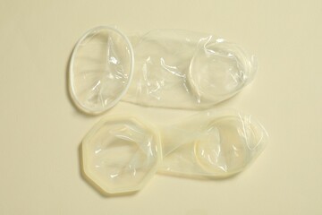 Unrolled female condoms on beige background, flat lay. Safe sex