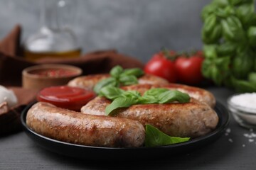 Tasty homemade sausages and basil leaves on grey wooden table, closeup