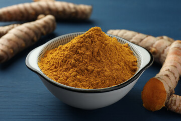Bowl with turmeric powder and raw roots on blue wooden table, closeup