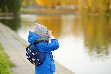 Little boy having fun during stroll in city park at sunny autumn day. Child exploring nature with...