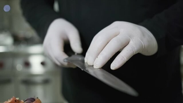 A chef in white gloves cuts garlic on a cutting board with a knife