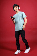 Full body of positive young man smiling at camera with holding smartphone and listening music...