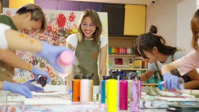 Group of Asian generation z people learning acrylic pouring art on canvas workshop at art studio. Young artist university student enjoy and fun creating colorful abstract modern art painting in class.