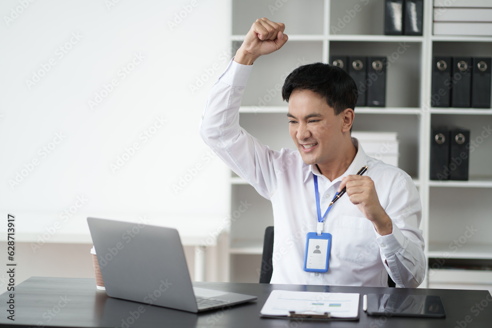 Wall mural Happy young businessman looking at laptop excited by good news online.