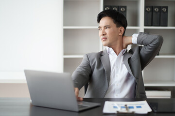 Young Asian businessman feeling pain, suffering from the neck pain after working for too long in the office room.