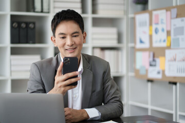 Smart young Asian businessman using smartphone while working in the office room.