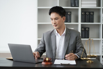 Young smart Asian lawyer working in his office room with laptop computer. Law firm concept.