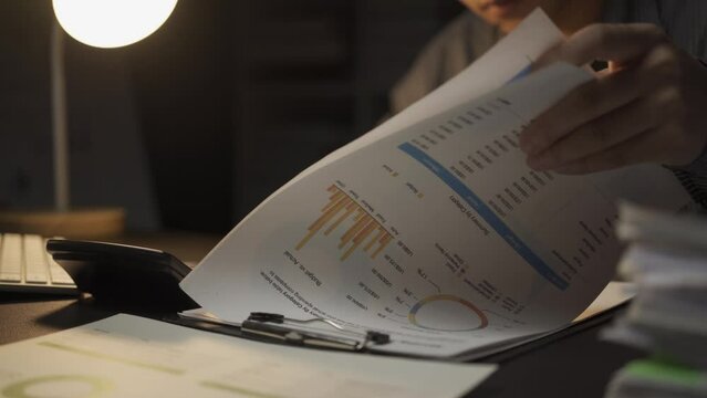 Asian male businessman working with financial documents and desktop computer till late at office, young man working overtime salaryman concept 4k