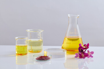 Some glassware of saffron and liquid in yellow color are surrounded a round-shaped podium. Decorated with Crocus flowers. Stage showcase on pedestal