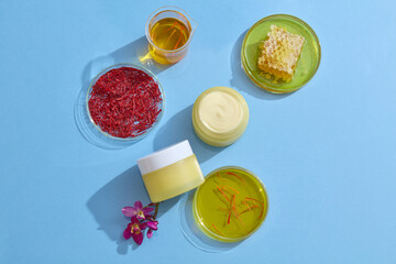 Against the blue background, yellow jars unlabeled decorated with petri dishes containing stigmas saffron, yellow essence and beeswax. Mockup for advertising cosmetic extracted from saffron