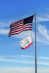 American flag and Californian flag wave in the breeze under a bright blue sky.