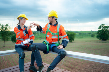 Two engineers discussing a project of wind turbine, They are sitting on a wooden platform, The concept of natural energy from wind.