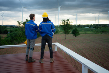 Back view of engineer and technician looking at wind turbines in the field before go in and check...
