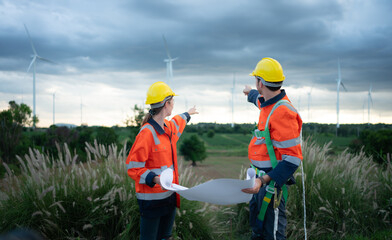 Two engineers working on a construction site with wind turbines in the background