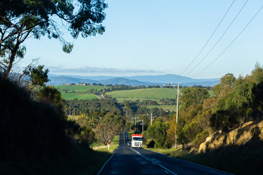 Truck driving on hilly road in green landscape on farmland outskirts of Melbourne