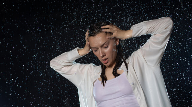 young woman in the rain, getting wet through, wet clothes and water running down her face. Emotional portrait in aqua studio