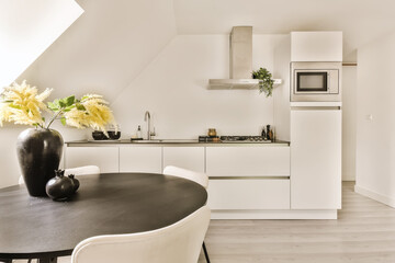 a kitchen with white cabinets and black counter tops in the center of the room, there is a vase of flowers on the table