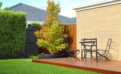 Typical Australian backyard features a lush artificial grass lawn, accompanied by a charming wooden decking area adorned with stylish outdoor furniture - 628731171