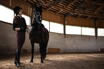 Equestrian sports. A young woman in a sports uniform, a rider and her horse in the arena, preparing...