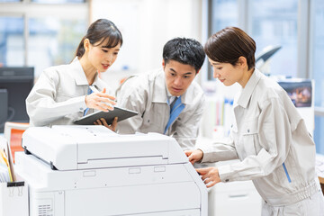 コピー機を点検する作業着を着た日本人
