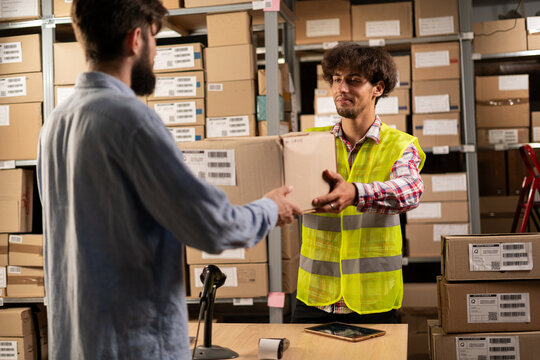 Male customer take online order at pick-up point. Online store warehouse worker giving parcel to man client at post office