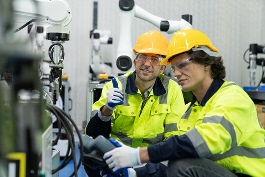 Two male automation machine engineer students studying training Programmable logic controller Technical Industrial Engineer control robotics with monitoring system software, Automation robot arm.