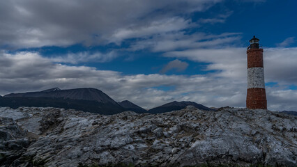 An old lighthouse Les Eclaireurs is installed on a rocky island in the Beagle Channel . A tall red-and-white striped tower against a background of blue sky and clouds. Argentina.
