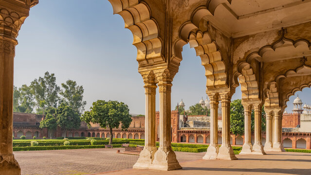 Ancient Indian architecture. Pavilion in the courtyard of the Red Fort. Carved columns with openwork arches against the blue sky. An old cannon is visible on the square. Trimming bushes in the garden - Powered by Adobe