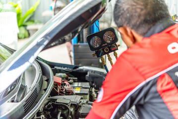 Car mechanic or serviceman refilling air condition and checking a air compressor for fix and repair problem at car garage or repair shop