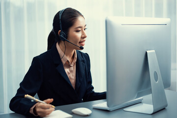 Asian call center with headset and microphone working on her laptop. Female operator provide...