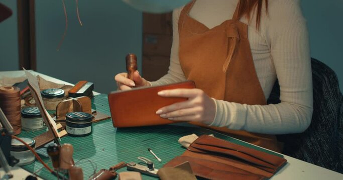 happy attractive ginger tailor enjoying polishing edges with slicker, burnisher creating sewing leather handmade wallet leathercraft, close up side view portrait.