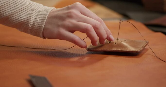 Skilled seamstress, female tailor puts needle with thread into cushion at workplace Slow motion closeup cropped shot, woman hands putting needle into handmade leather cushion, craft