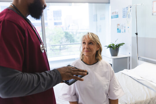 African american male doctor talking to senior caucasian female patient, using tablet