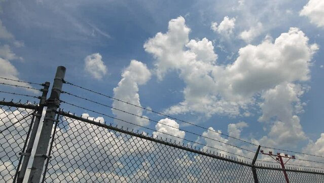 Airplane Crosses Low Overhead With Barbed Wire Fence In Foreground
